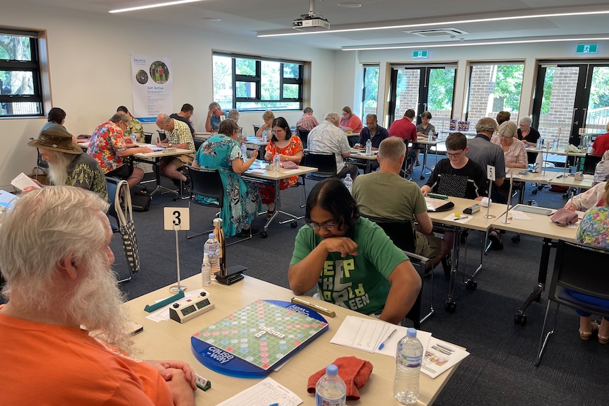 People play scrabble in pairs in a small room at folding tables