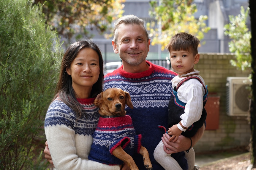 A woman, man and child pose for a photo with a small dog.