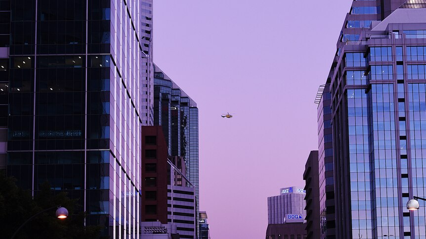 Looking down St George's Terrace at dusk, a helicopter hovers between the skyscrapers.