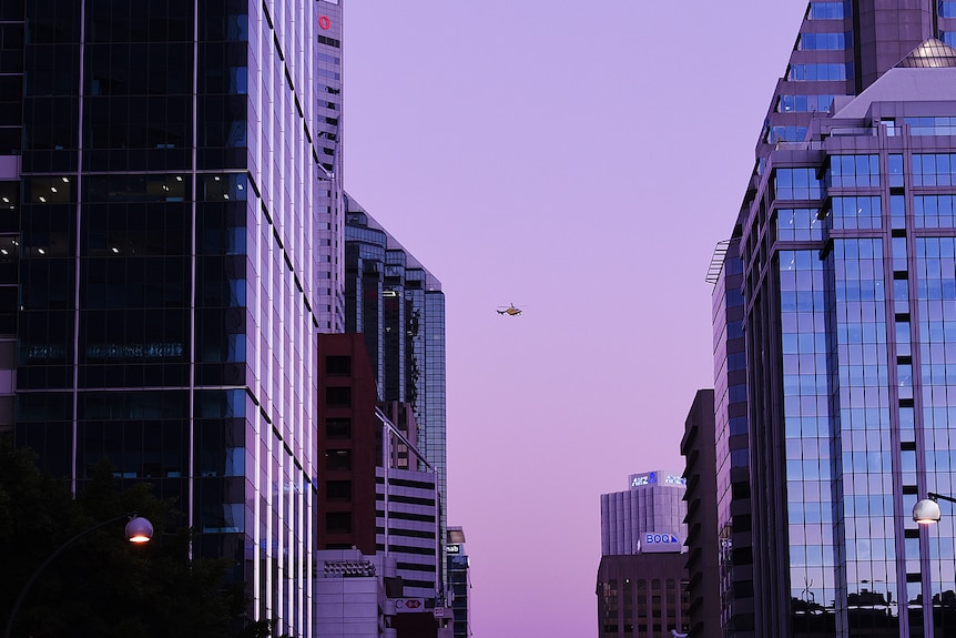 Looking down St George's Terrace at dusk, a helicopter hovers between the skyscrapers.