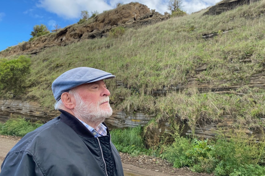 A man in a woollen cap stands beside a volcanic quarry wall