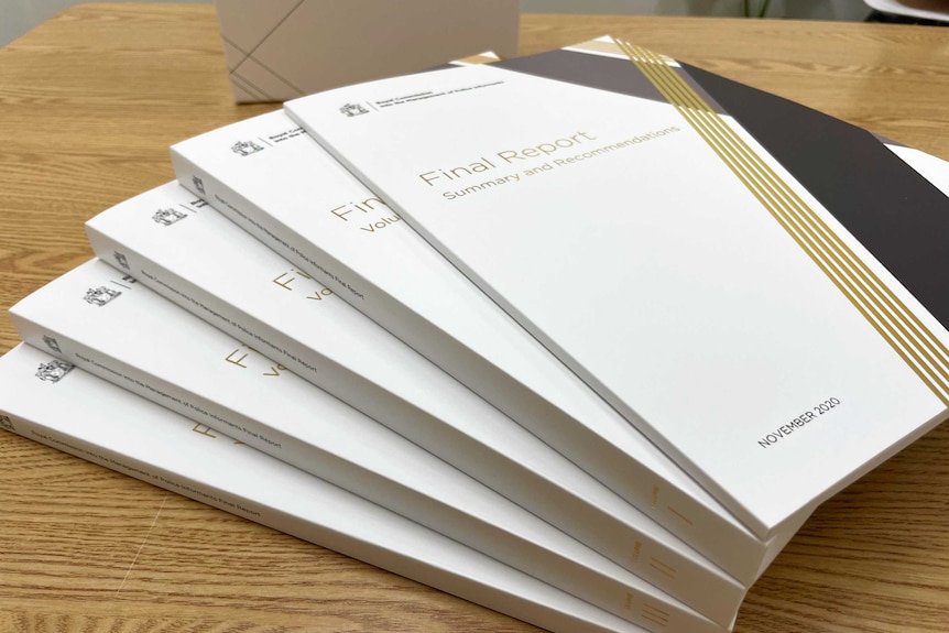 Five volumes of the final report of the Lawyer X royal commission fanned out on a table.