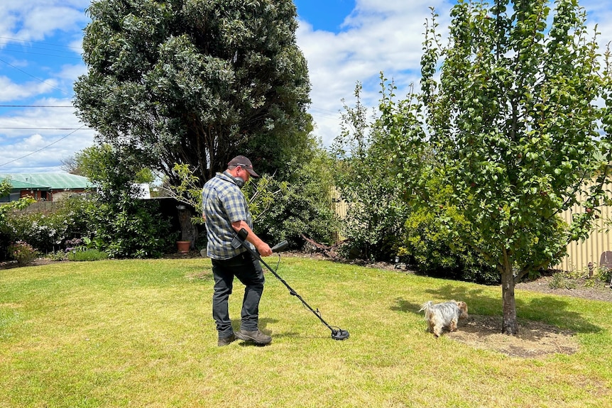 A man uses a metal detector in a sunny backyard.