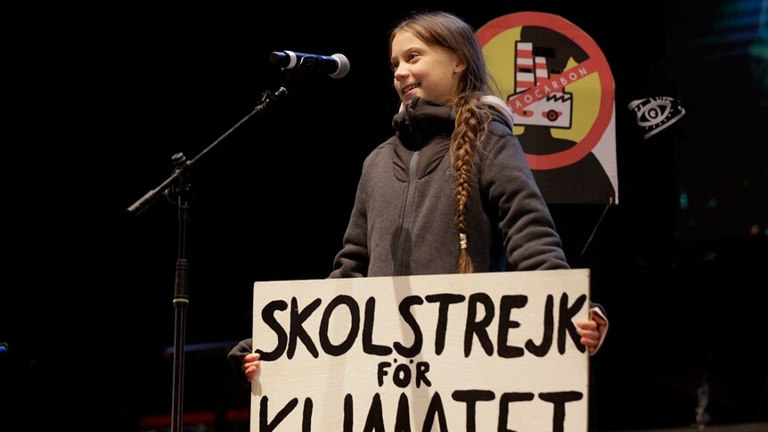 Greta Thunberg wit h a sign speaking in a microphone.