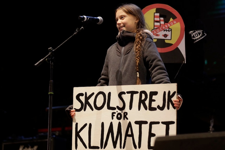 Greta Thunberg wit h a sign speaking in a microphone.
