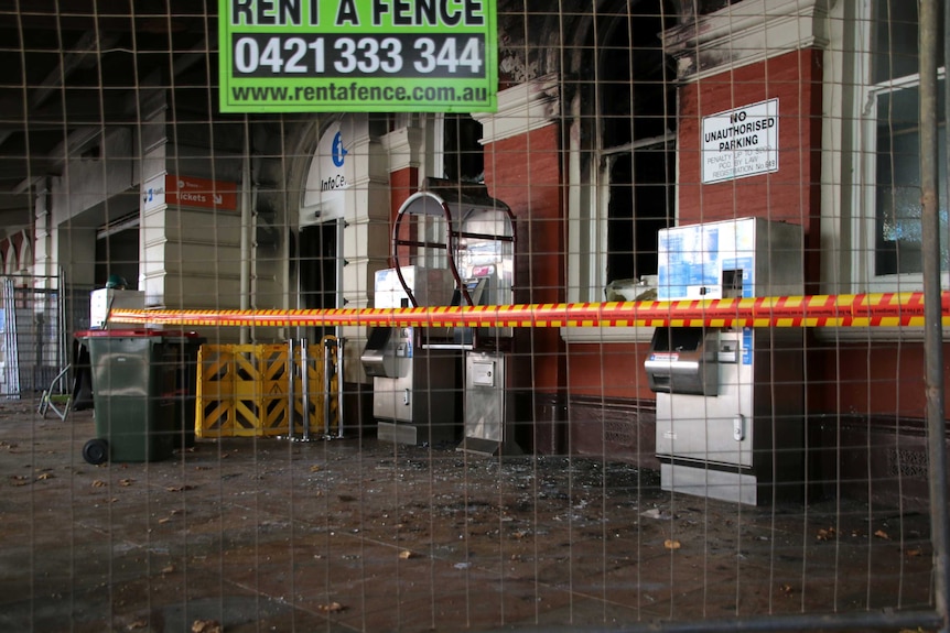 The wall and roof of the entrance to the train station is blackened, and a window smashed.