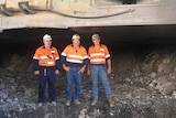 Three men in hard hats and high-vis standing in a line at a coal mine.