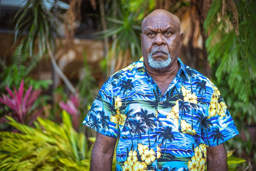 A man looking serious, wearing a floral shirt.