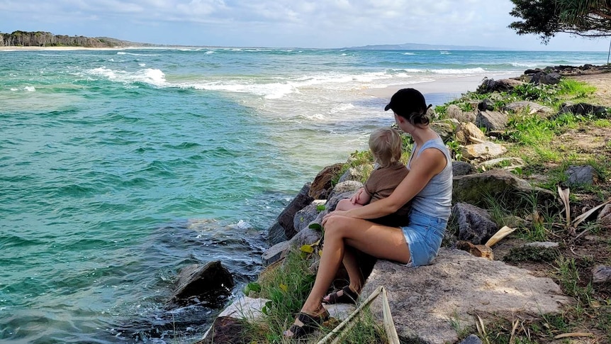 Kellie sitting on a rock holding Lane looking at water in Noosa