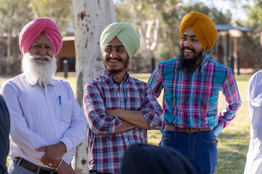 A group of four men in turbans stand outside by trees, smiling.  
