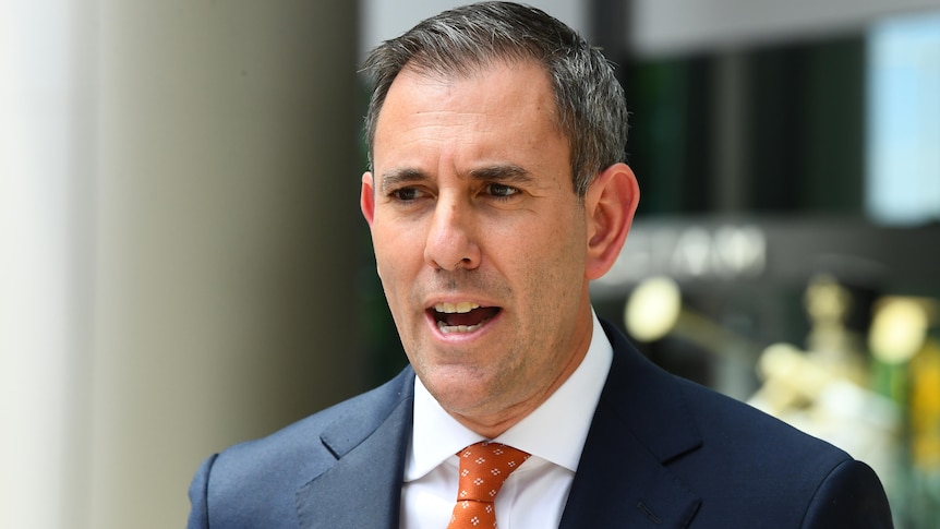 A close up of Jim speaking in a suit and orange tie outside a building during the day.