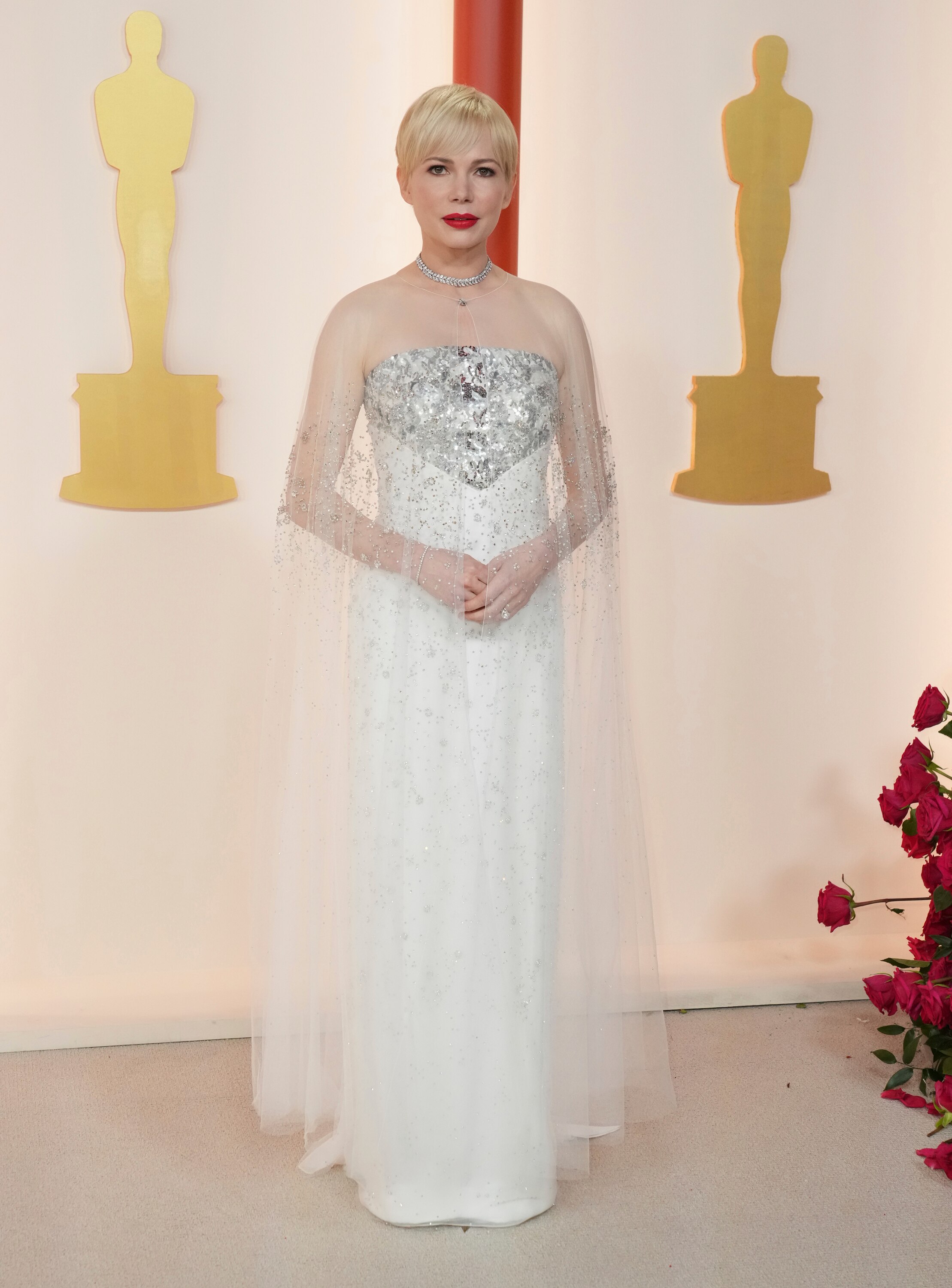 Michelle Williams wearing a strapless white floor-length gown with silver metallic detailing on the bust and a sheer white cape