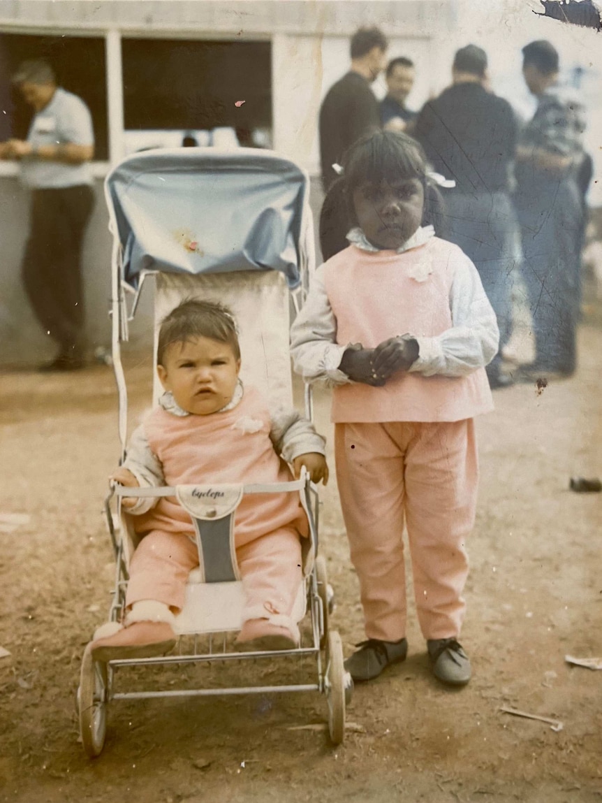 A historic photo of Leanne Liddle as a young child in a pram with her older sister Jenny standing next to her.