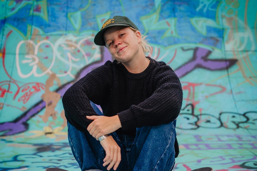 Exterior scene a smiling Poppy Starr Olsen pictured sitting on a skateboard in a concrete bowl