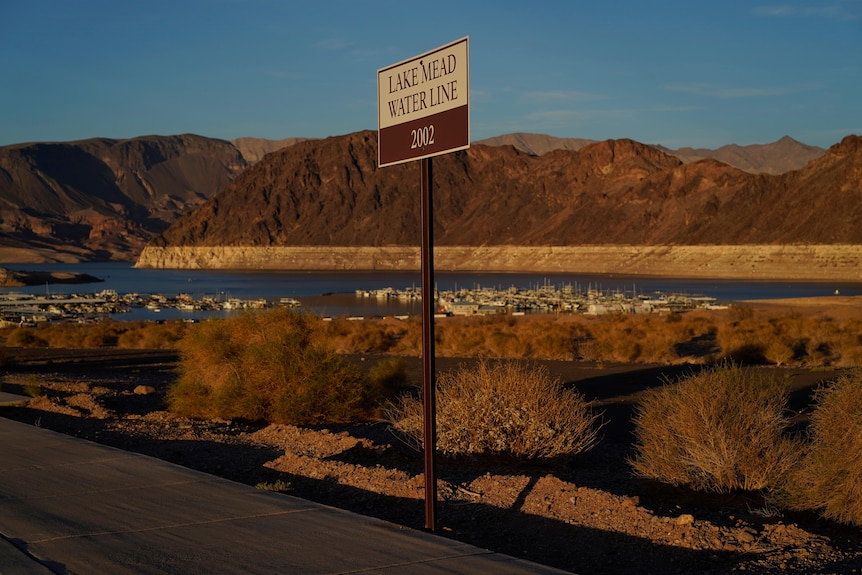 A roadside sign reading "Lake Mead Water Line 2002". In background can see lake, boats and a mountain range on horizon.