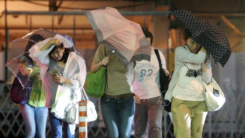 People try to hold onto their umbrellas under heavy winds and rain brought by typhoon Jelawat in Japan.