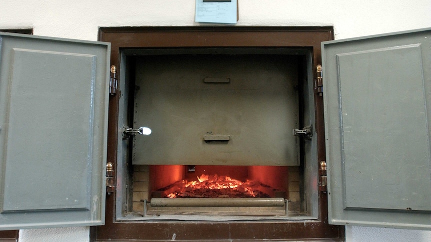 A cremation oven partially open with hot coals in the bottom.