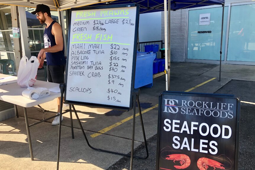 Marque stand, seafood sales and seafood prices on a white board with a worker in the background.