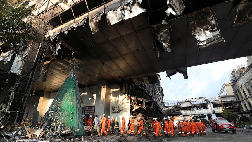 Rescue experts in orange kit walk through a ruined building.