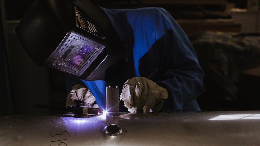 A person wearing a welding masks and gloves welds.