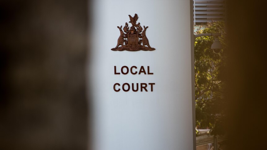 A coat of arms and sign saying 'Local Court' on a column outside a courthouse. 