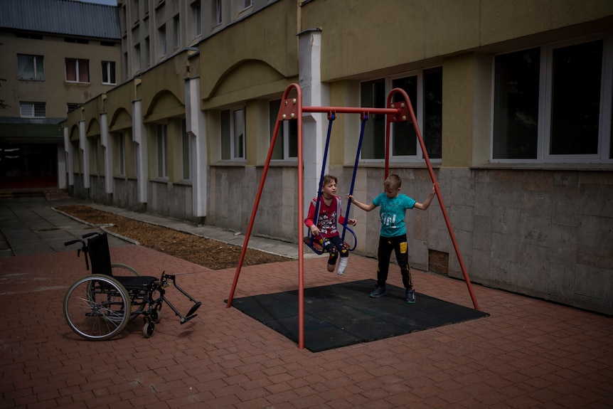 A girl with two amputated legs sits on a swing while a boy pushes the swing