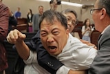 A man with an extremely angry face is held back by security guards inside Hong Kong's parliament.