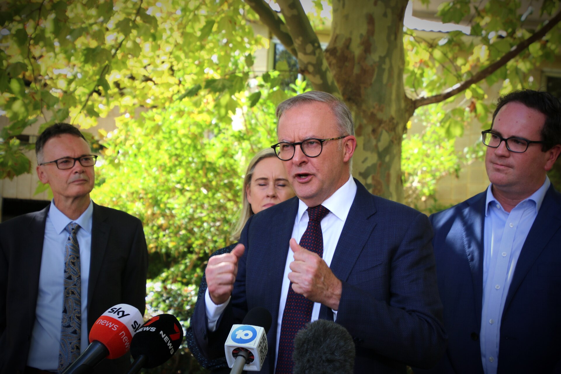 The Prime Minister stands in a leafy green area holding a press conference