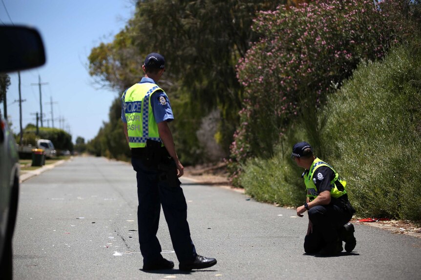 One police officer kneels on the road, another stands, as they examine the scene.