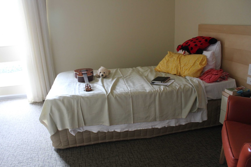 A hospital bed with a ukelele and stuffed animals sitting on top of the covers.