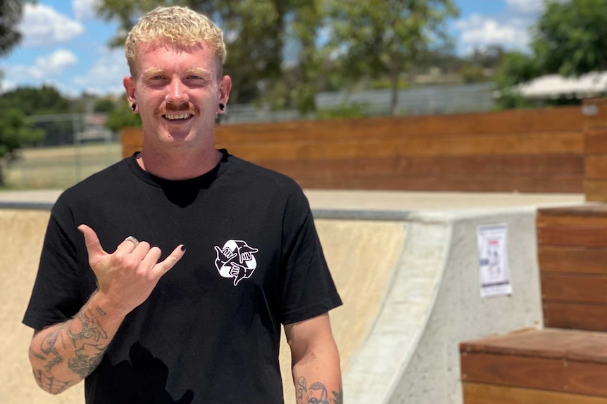 Jayden smiles to the camera, positioned to the left hand side. Skate ramp is positioned in the background.