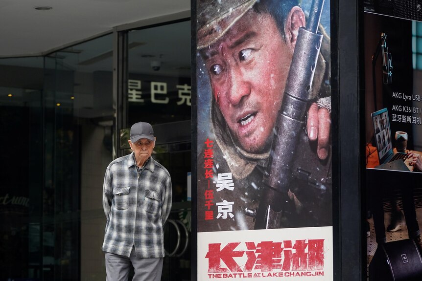 An elderly Chinese man walks past a movie poster featuring a young Chinese soldier holding a gun