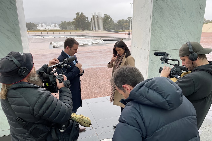 Two camera operators filming a man and a woman with foggy background of Old Parliament House in Canberra.