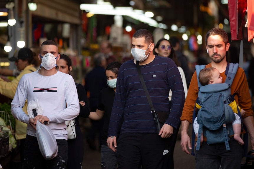 People wearing face masks walking along a street in Israel.