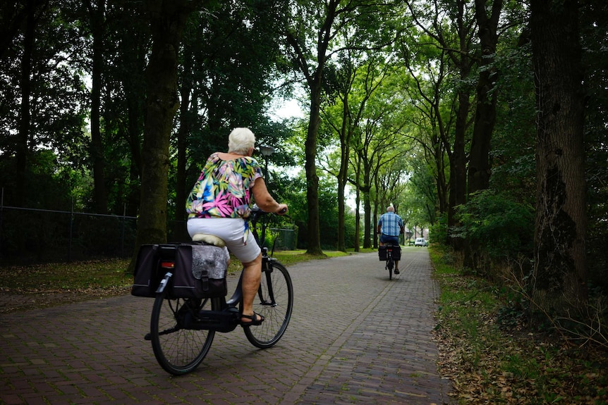 A woman and a man ride bicycles on a cobbled path.