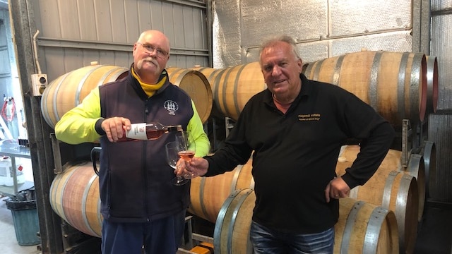 Peter McGlashan pours Martin Cooper a glass of wine at Ridgemill Estate near Stanthorpe in front of wine barrels, June 2020.