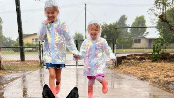 two little girls in pink gum boots and rain jackets play in rain