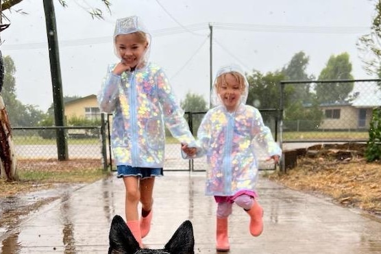 two little girls in pink gum boots and rain jackets play in rain