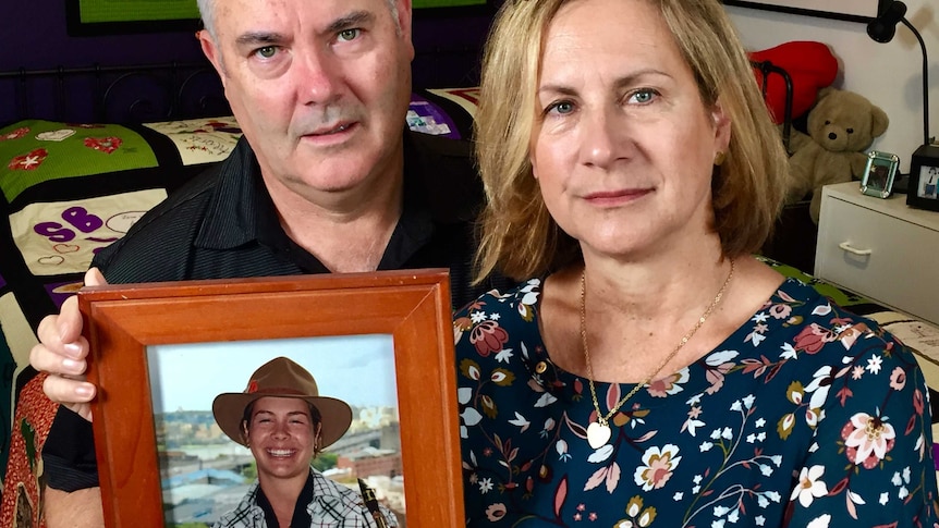 A mother and father hold up a photo of their daughter.