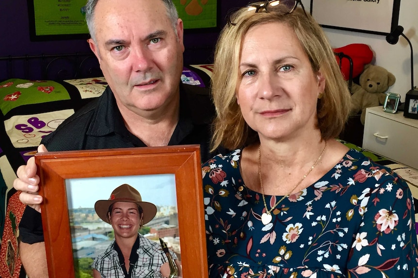 A mother and father hold up a photo of their daughter.