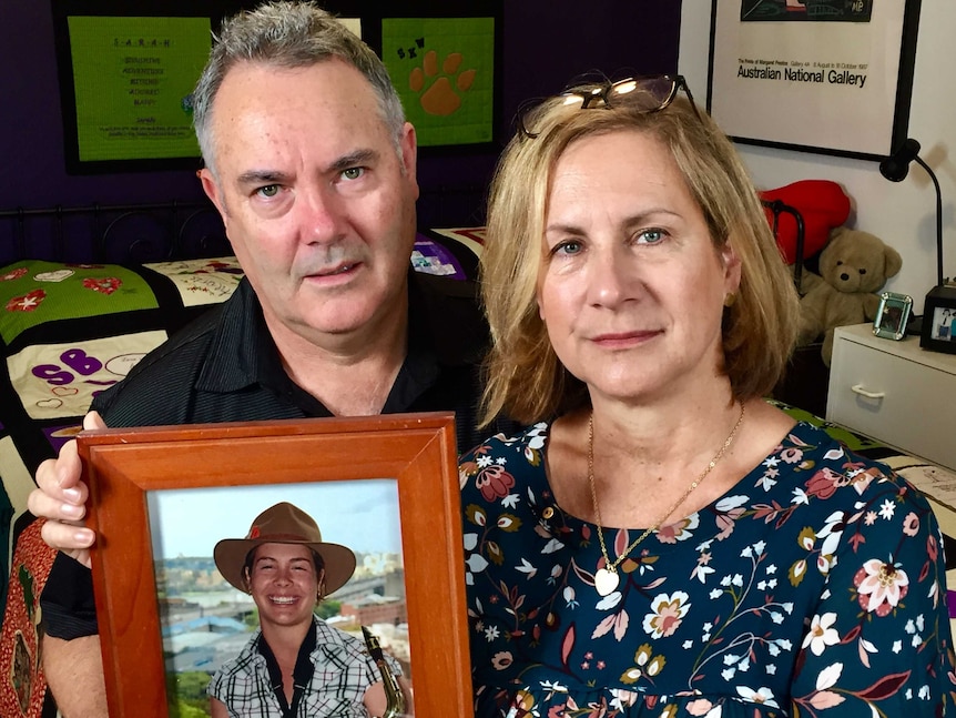 A mother and father hold up a photo of their daughter.