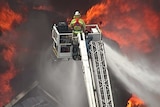 A firefighter on a crane hosing a fire.