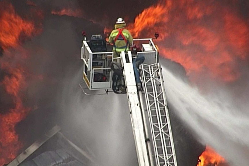 A firefighter on a crane hosing a fire.