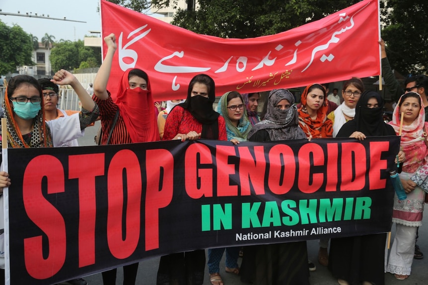 A group of Pakistani women stand behind a banner that reads 'Stop Genocide in Kashmir'.