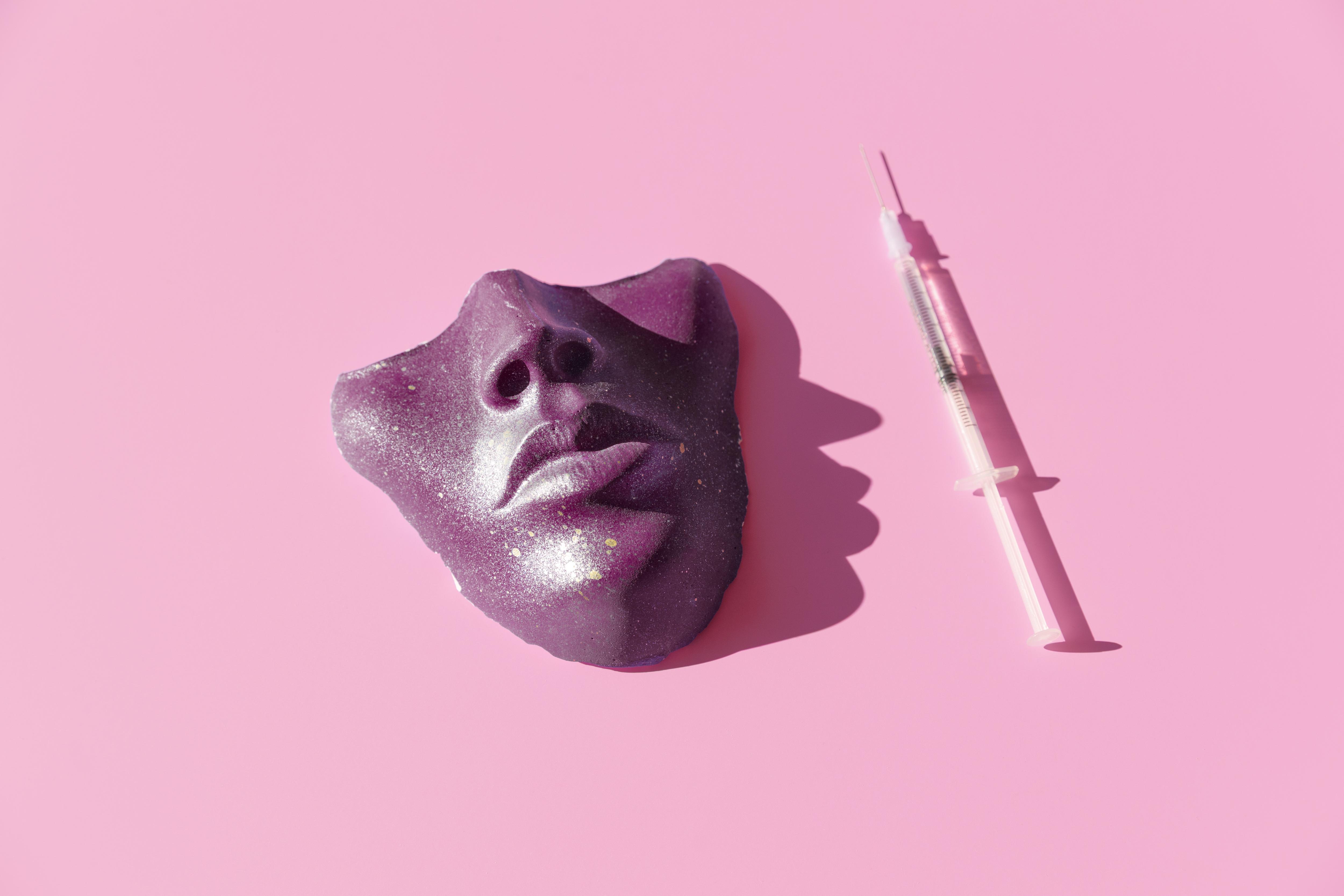 Purple colored syringe and face mask on the pink background