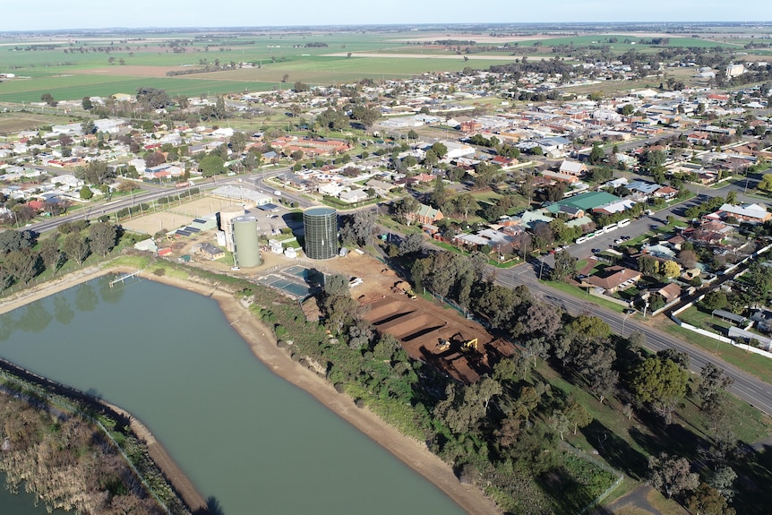 an aerial view of a large dam adjacent to trees, a water tower and town
