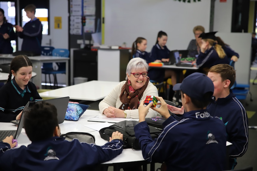 Older lady sitting at a desk engaging with school children