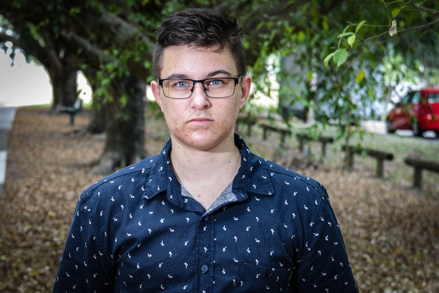 Transmasculine person Ash Polzin wearing glasses standing in a park.