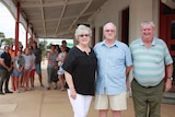 Three people stand in front of a crowd under the verandah of the Heyfield Railway Hotel.