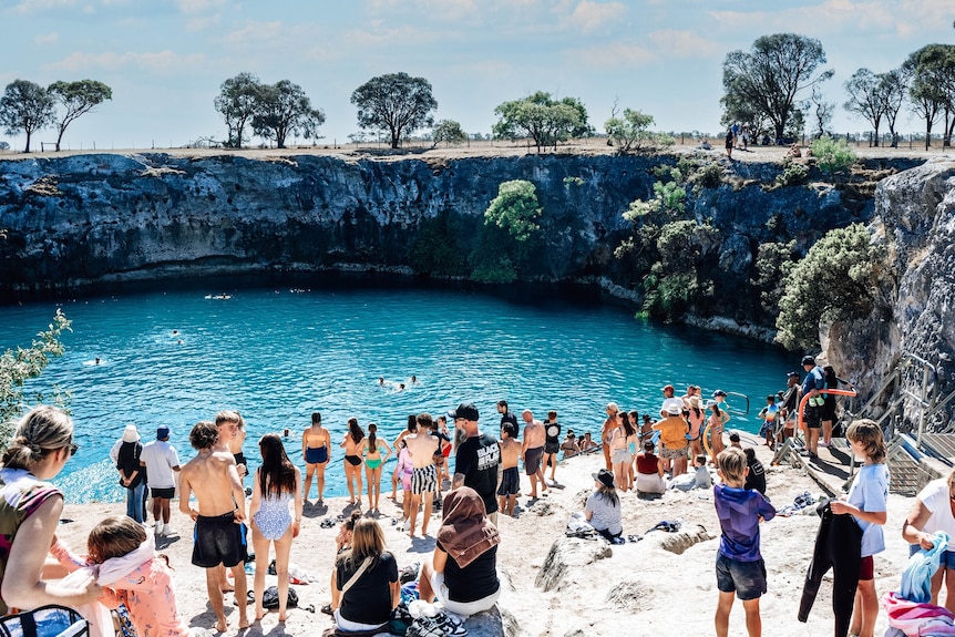 People in swimming gear standing on the edge of a sinkhole with green water